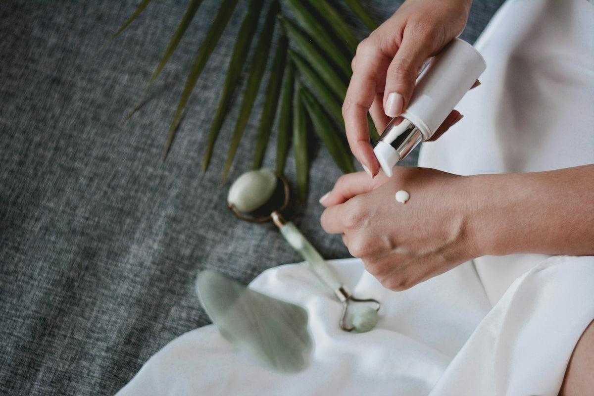 A person applying lotion to their hand with a jade roller and gua sha