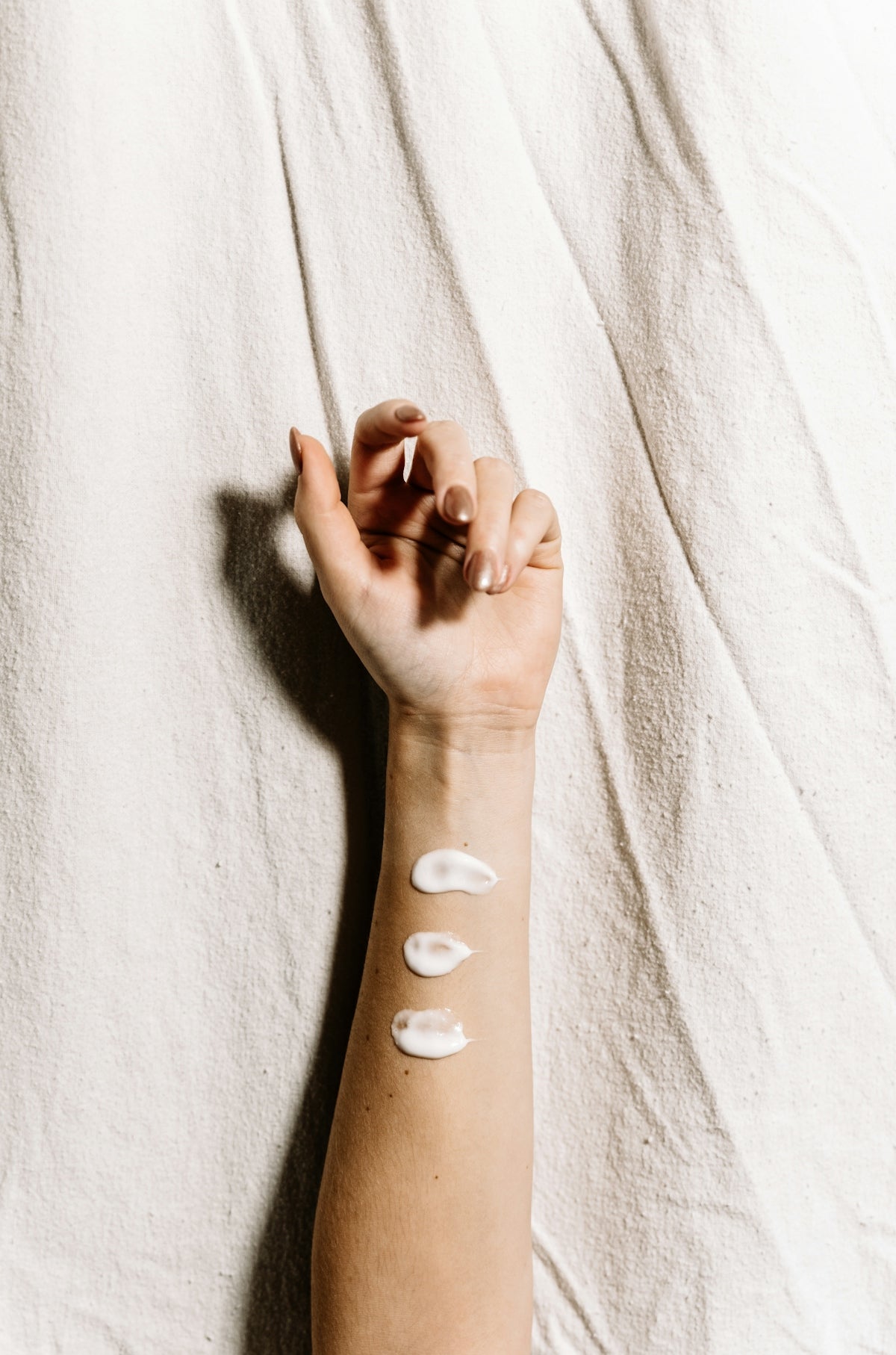 A person's arm with three dabs of white cream on a textured fabric